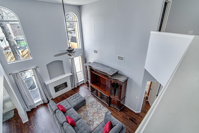 living area featuring a fireplace, visible vents, a ceiling fan, and wood finished floors