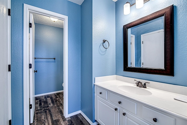 bathroom with toilet, vanity, a textured ceiling, wood finished floors, and baseboards