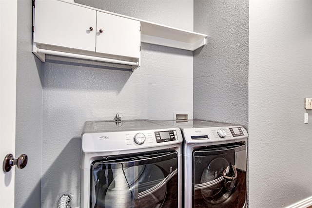 washroom with a textured wall, washing machine and dryer, and cabinet space