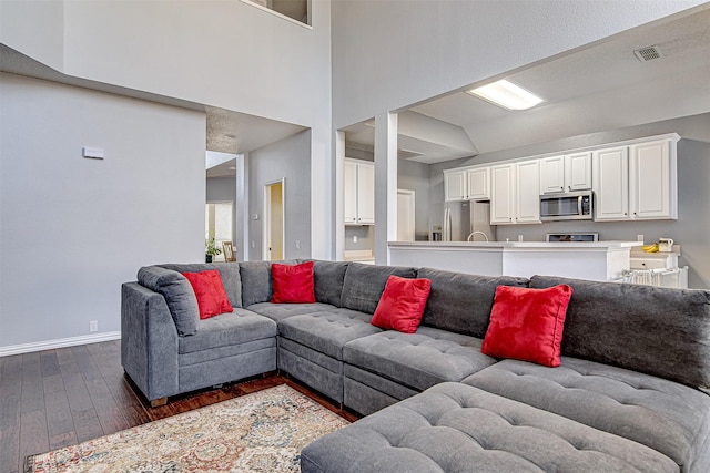 living room with dark wood-style flooring, a towering ceiling, visible vents, and baseboards