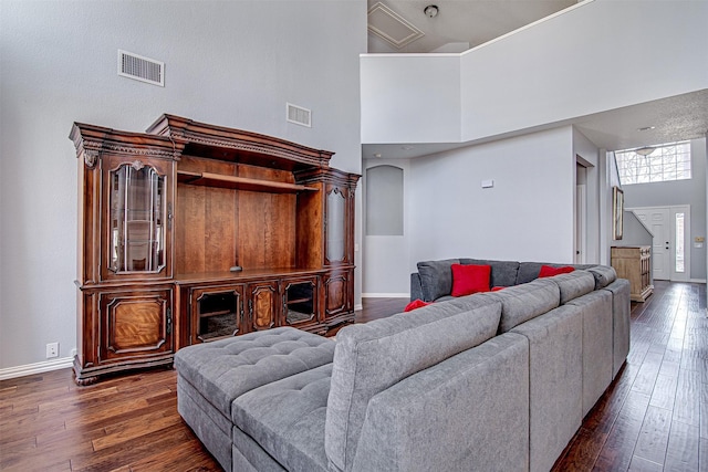 living area featuring dark wood-type flooring, visible vents, a towering ceiling, and baseboards