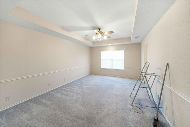 empty room with ceiling fan, carpet flooring, visible vents, baseboards, and a tray ceiling