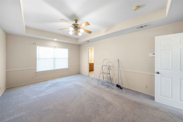 unfurnished room featuring visible vents, baseboards, light colored carpet, ceiling fan, and a tray ceiling