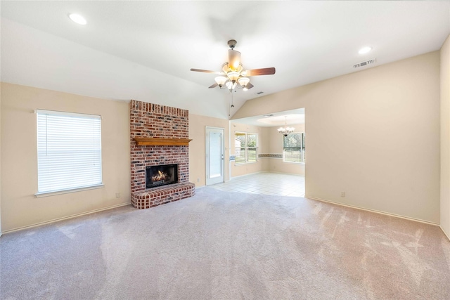 unfurnished living room featuring visible vents, lofted ceiling, carpet floors, a brick fireplace, and ceiling fan with notable chandelier