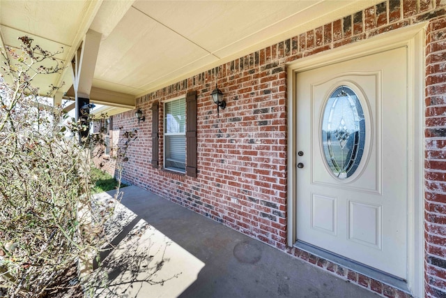 entrance to property with a porch and brick siding