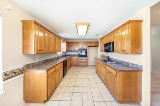 kitchen featuring brown cabinets, light tile patterned floors, dark countertops, a sink, and black appliances