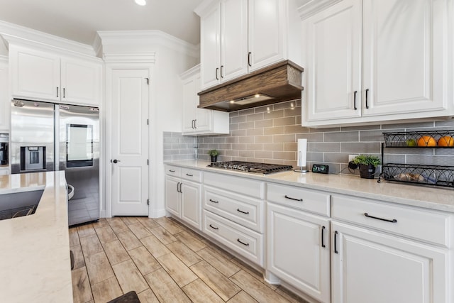 kitchen with appliances with stainless steel finishes, wood tiled floor, white cabinetry, and under cabinet range hood