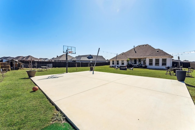 view of sport court with a yard, basketball hoop, and fence