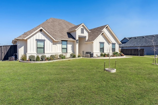 modern farmhouse style home featuring roof with shingles, a front lawn, board and batten siding, and fence