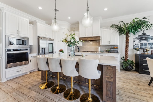 kitchen with a breakfast bar area, under cabinet range hood, stainless steel appliances, tasteful backsplash, and crown molding