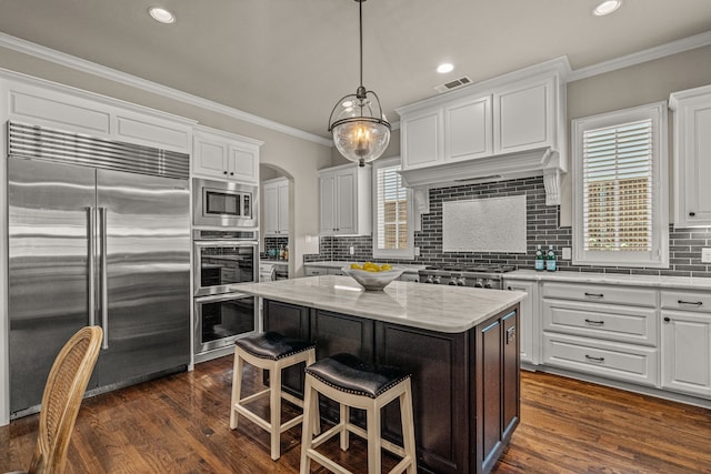 kitchen featuring visible vents, built in appliances, ornamental molding, arched walkways, and white cabinetry