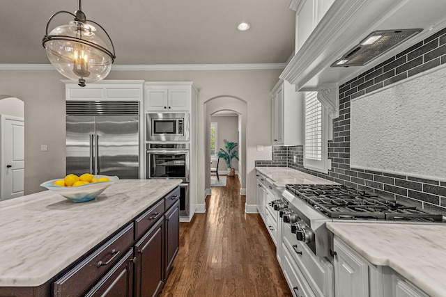 kitchen with ventilation hood, arched walkways, ornamental molding, white cabinets, and built in appliances