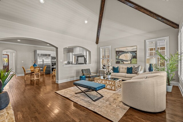 living area featuring arched walkways, vaulted ceiling with beams, baseboards, and wood finished floors