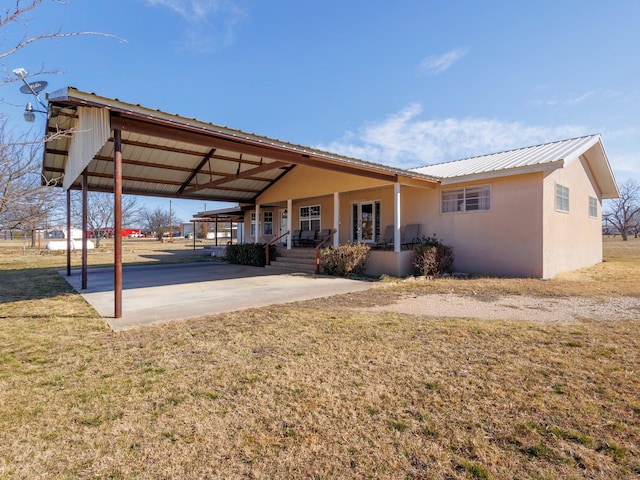 back of house featuring metal roof, covered porch, a lawn, and stucco siding