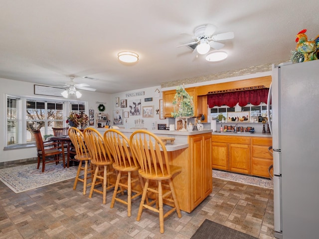 kitchen with a breakfast bar area, light countertops, freestanding refrigerator, a sink, and ceiling fan