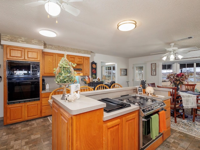 kitchen featuring a kitchen island, visible vents, light countertops, black appliances, and stone finish floor