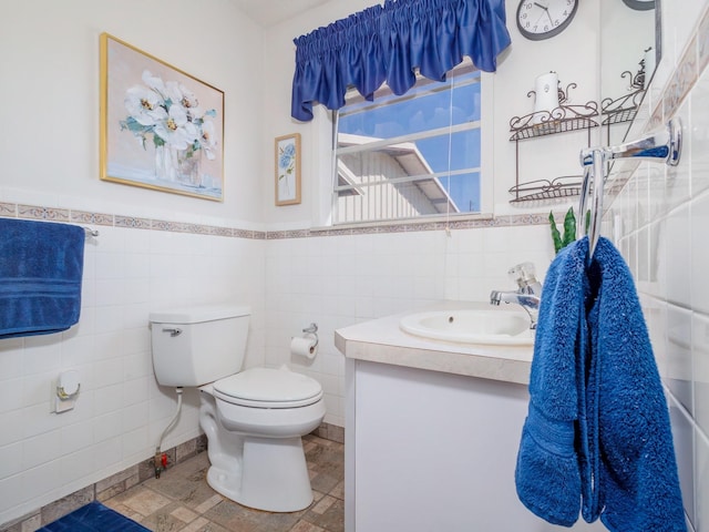 bathroom with tile walls, a wainscoted wall, vanity, and toilet