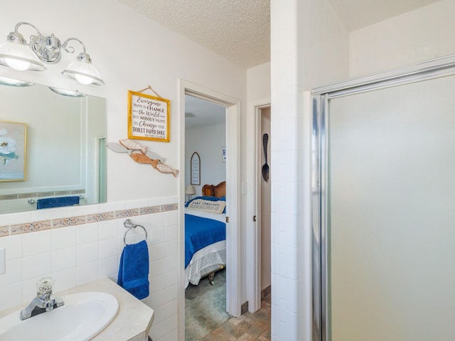 bathroom featuring a wainscoted wall, tile walls, connected bathroom, a sink, and a textured ceiling