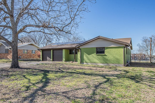 view of front of home with brick siding, solar panels, an attached garage, fence, and a front lawn