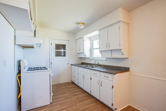 kitchen featuring wainscoting, dark countertops, gas range gas stove, light wood-style floors, and a sink