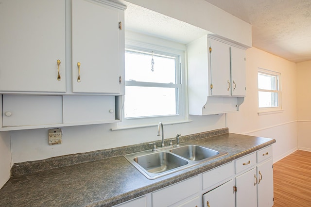 kitchen featuring dark countertops, light wood-style flooring, white cabinets, a sink, and a textured ceiling