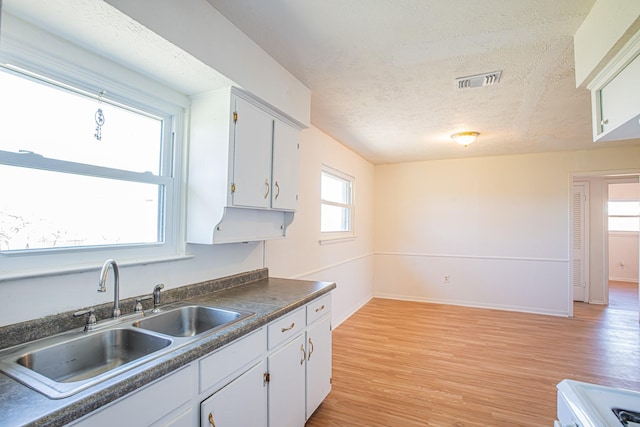 kitchen featuring a sink, visible vents, white cabinetry, light wood-type flooring, and dark countertops