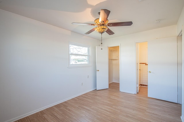 unfurnished bedroom with a closet, a spacious closet, light wood-style floors, a ceiling fan, and baseboards