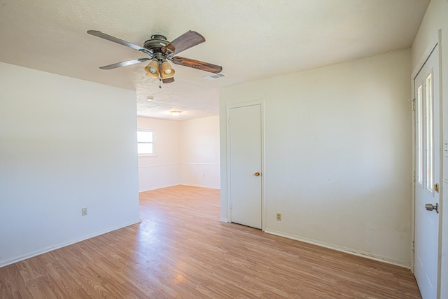 spare room featuring a textured ceiling, ceiling fan, visible vents, baseboards, and light wood finished floors