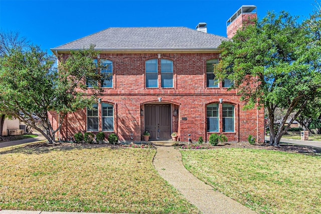 view of front of property with a shingled roof, a front yard, a chimney, and brick siding