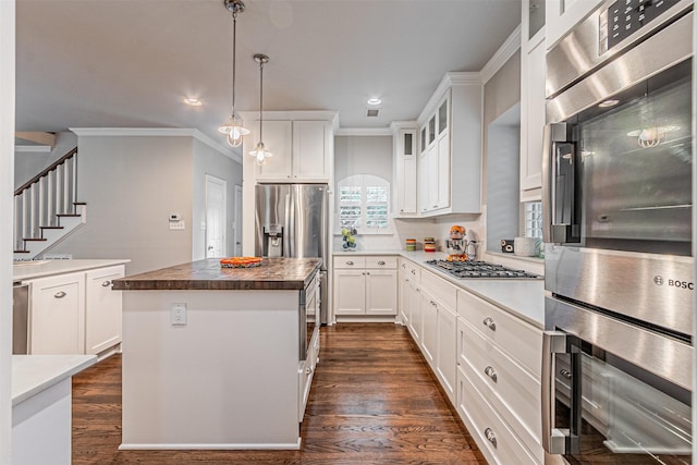 kitchen with stainless steel appliances, ornamental molding, dark wood-type flooring, and a kitchen island