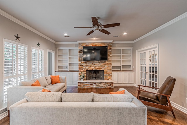 living area with a stone fireplace, baseboards, built in features, dark wood-style floors, and crown molding