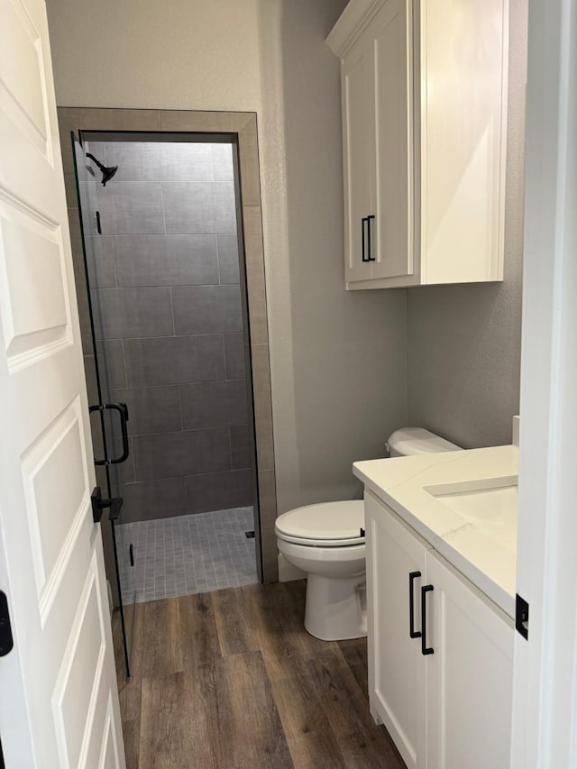 bathroom featuring toilet, a shower stall, wood finished floors, and vanity