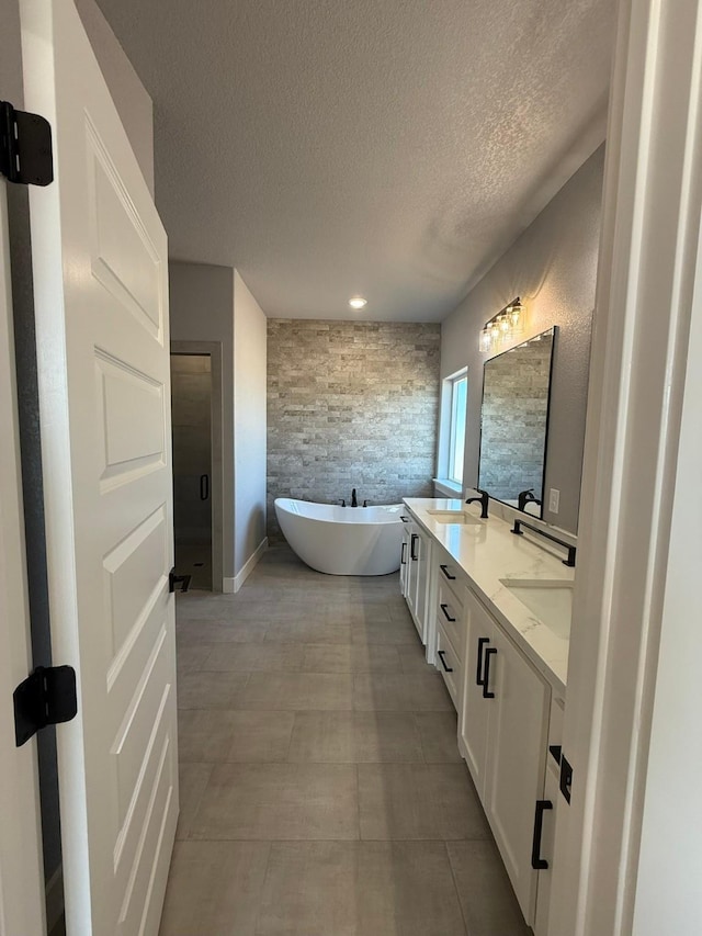 bathroom with double vanity, a sink, a textured ceiling, and a freestanding bath