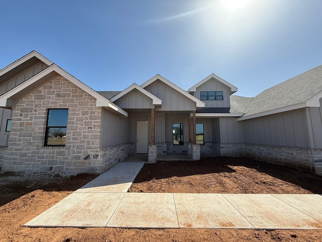 view of front facade with stone siding, board and batten siding, and roof with shingles