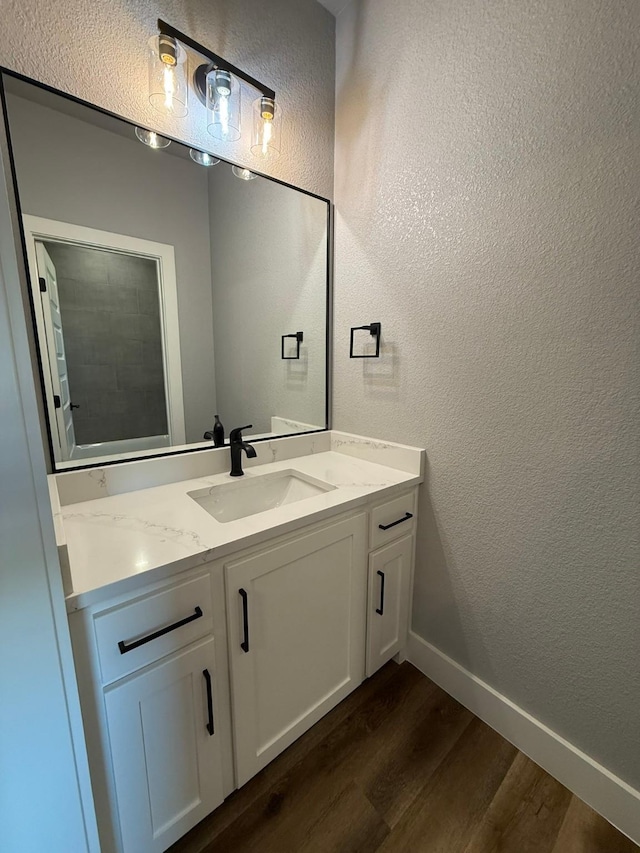 bathroom with a textured wall, vanity, baseboards, and wood finished floors