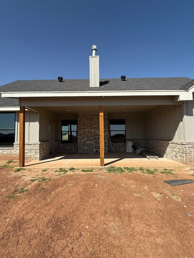 back of house with a patio, brick siding, board and batten siding, and a shingled roof