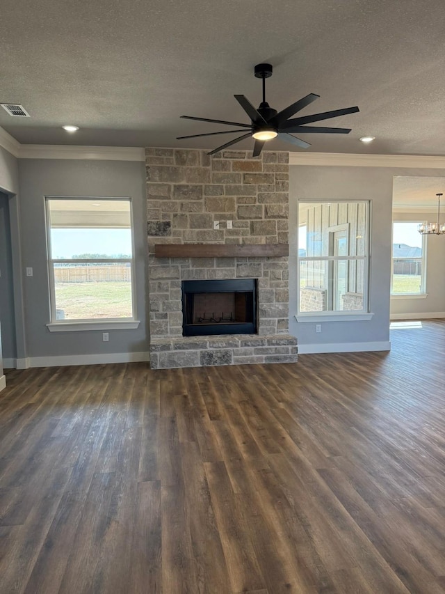 unfurnished living room featuring a textured ceiling, a stone fireplace, wood finished floors, baseboards, and crown molding