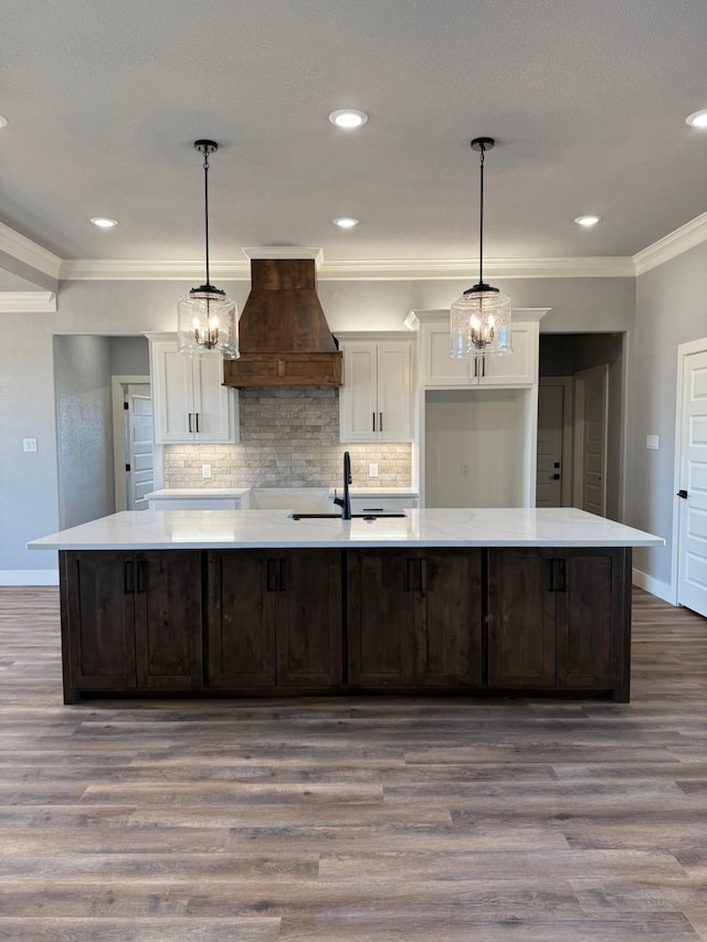 kitchen with a spacious island, a sink, white cabinetry, light countertops, and custom exhaust hood