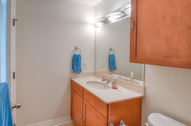 bathroom with toilet, a textured wall, and vanity