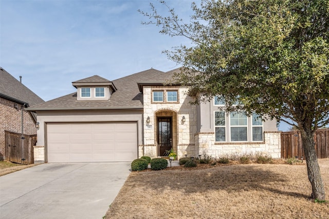 view of front of home with an attached garage, a shingled roof, fence, stone siding, and driveway