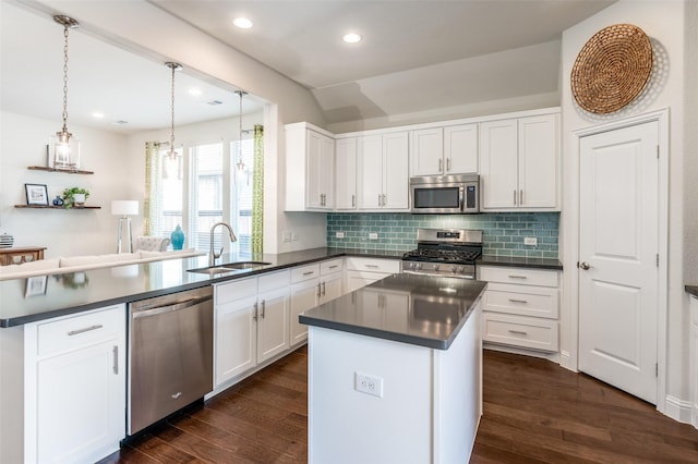 kitchen with dark countertops, dark wood-type flooring, a peninsula, stainless steel appliances, and a sink