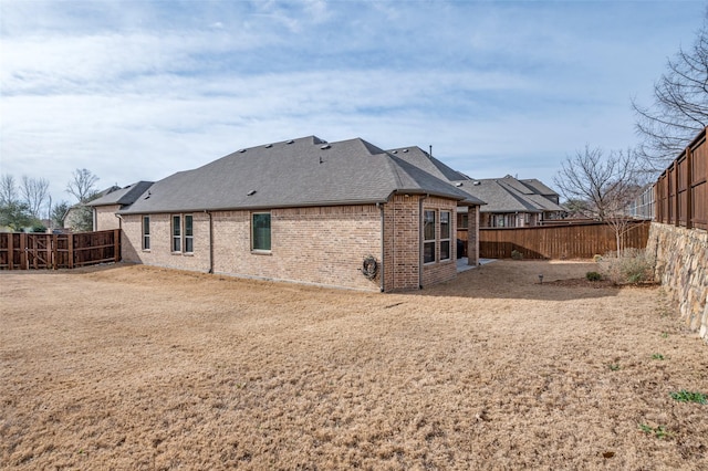 rear view of property with brick siding, a shingled roof, and a fenced backyard