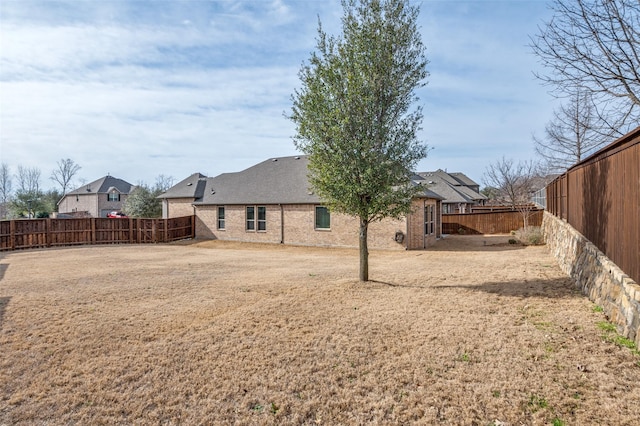 back of house featuring a yard, a fenced backyard, a shingled roof, and brick siding