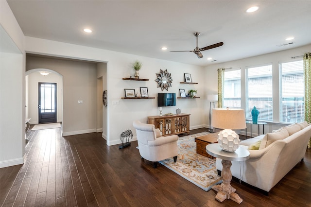 living room featuring a healthy amount of sunlight, visible vents, arched walkways, and dark wood-type flooring