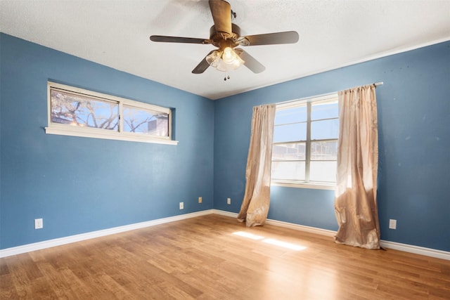 empty room featuring a healthy amount of sunlight, a ceiling fan, baseboards, and wood finished floors