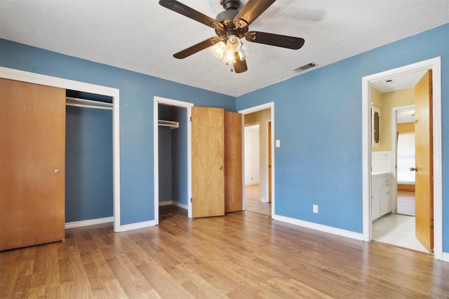 unfurnished bedroom with ceiling fan, wood finished floors, visible vents, baseboards, and multiple closets