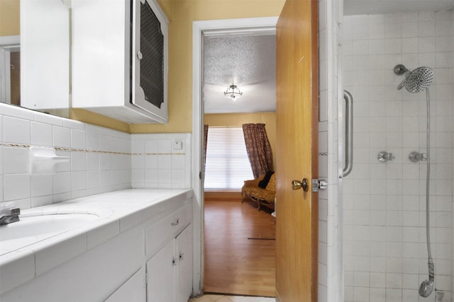 full bath with tasteful backsplash, a textured ceiling, vanity, wood finished floors, and tiled shower