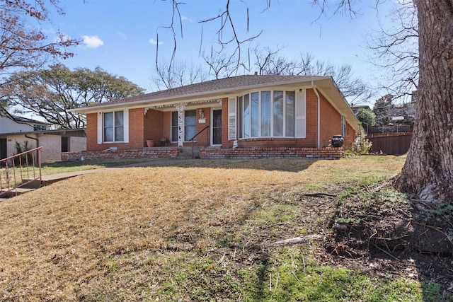 view of front of property featuring brick siding, fence, and a front lawn