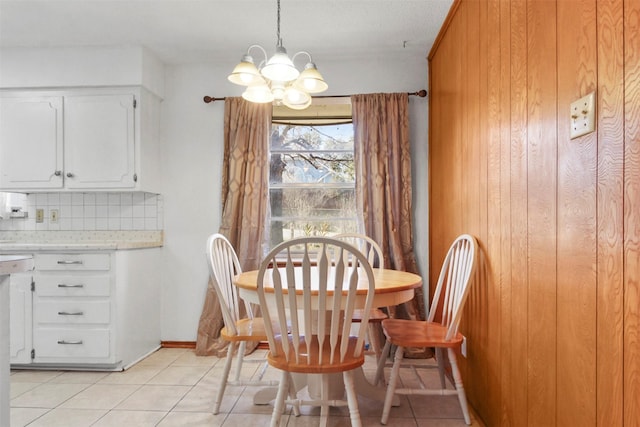 dining room featuring light tile patterned floors, wood walls, baseboards, and an inviting chandelier