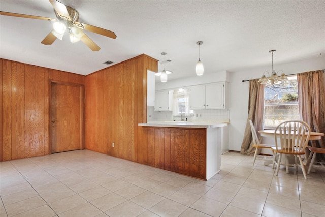 kitchen with light tile patterned flooring, wooden walls, a peninsula, white cabinets, and light countertops